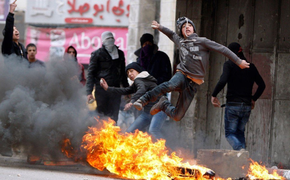 23. A Palestinian boy throws a stone towards Israeli soldiers as he jumps over burning tyres - March 17, 2014.