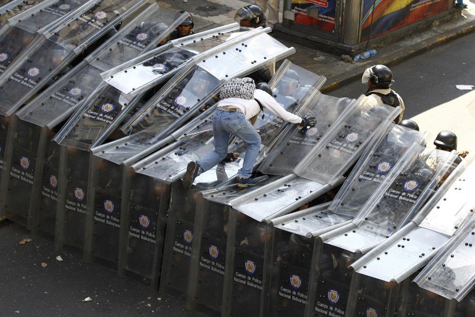 40. A protestor jumps on a shield wall formed by riot police during a protest against Venezuela’s President Nicolas Maduro’s government in Caracas - February 12, 2014.