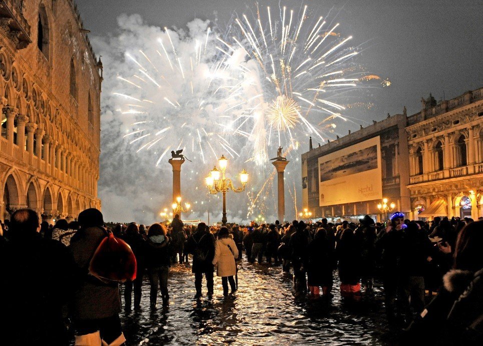 People watch New Year's Eve fireworks over Venice's St. Mark square flooded by high water, early Friday, Jan. 1, 2010. The phenomenon of high water, which floods the Venice lagoon, occurs mainly between autumn and spring when tides are reinforced by seasonal winds. (AP Photo/Luigi Costantini)