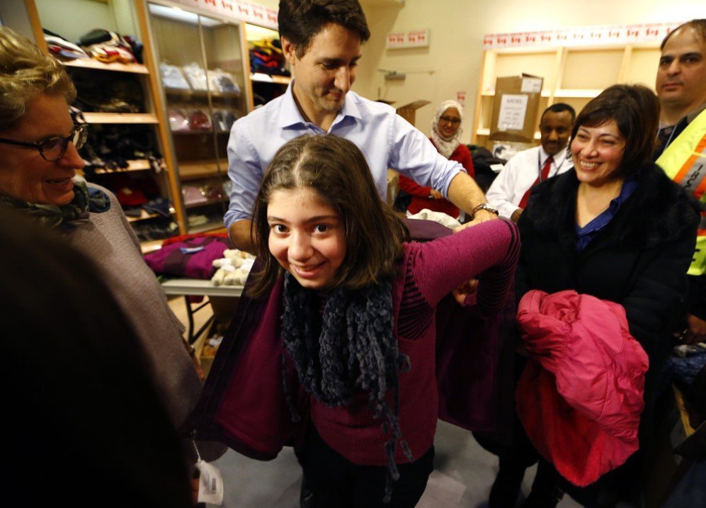 Canada’s Prime Minister Justin Trudeau helps a young Syrian refugee try on a winter coat after she arrived with her family from Beirut in Mississauga, Ontario, Canada –Dec. 11, 2015