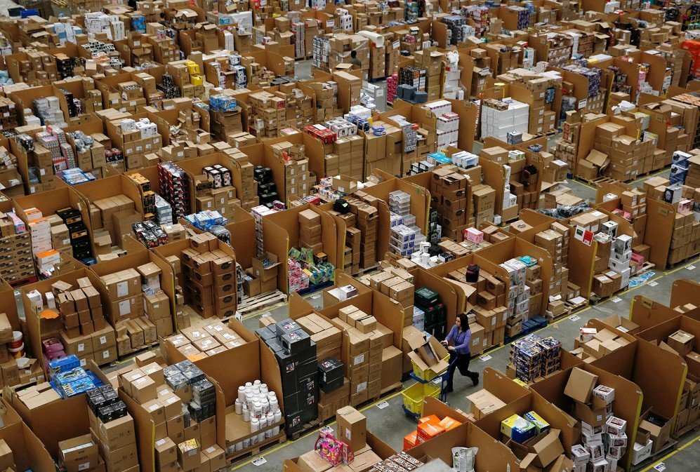 Workers walk along aisles of goods stored inside an Amazon.co.uk fulfillment centre in Hemel Hempstead, London – Nov. 25, 2015.
