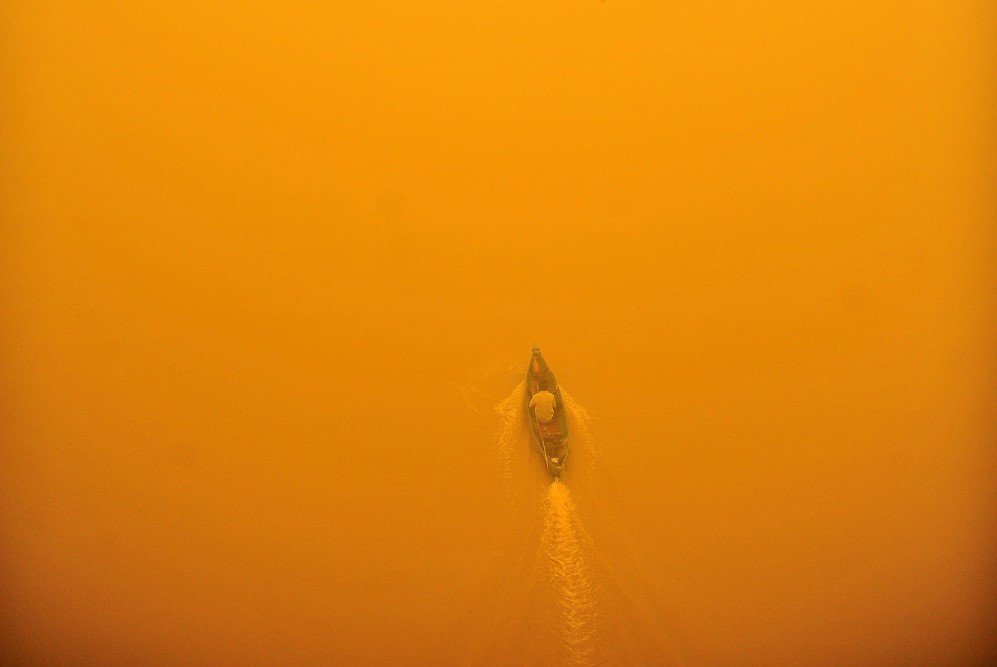 An Indonesian man rides a wooden boat through thick yellow haze on Kahayan River in Indonesia – Oct. 23, 2015.
