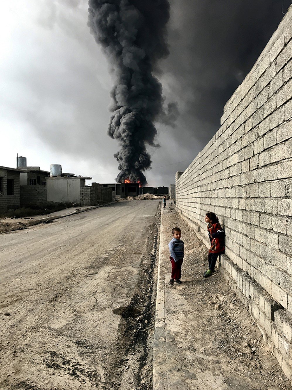 Children roam the streets in Qayyarah near the fire and smoke billowing from oil wells, set ablaze by ISIS militants.