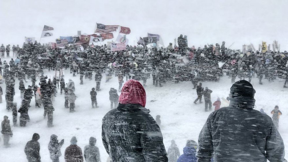 These pictures were taken on December 5th, 2016 at Standing Rock, North Dakota. That day the water protectors, the people standing up for the Sioux tribe were supposed to get evicted by the Morton County Sheriff’s Department. Thousands of veterans came to the aid of those of us who were protesting. They told us that they had vowed to protect this country from all enemies, foreign and domestic. President Obama announced that the Dakota Access Pipeline had to be halted until an investigation was made. The veterans still marched on that afternoon and made sure to let everyone know that they were there helping protect Standing Rock. Mother Nature stepped in that day with a blizzard of 40 to 50 mph winds with temperatures of -30F. The height of the storm and the march was captured with the photo that was selected for first place. Everyone there stood until it was physically impossible to continue. Shortly after that picture was taken everyone had to go back to camp and the officers on the other side of the bridge had to leave as well. It was a great reminder of who truly was in charge.