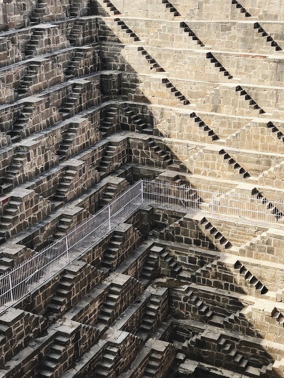 This photo was taken when I was traveling in India. Chand Baori consists of 3,500 narrow steps over 13 storeys. It extends approximately 30 meters into the ground making it one of the deepest and largest stepwells in India. I marveled these elegant stepwells and shadows, I immediately took out my camera and captured this beautiful scene before it was gone.