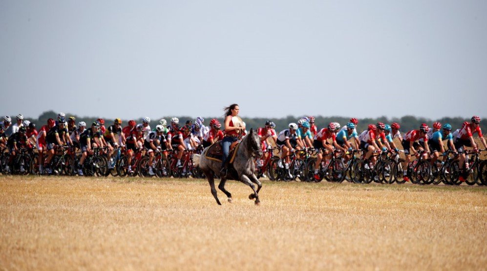 a woman rides a horse as the pack of riders from the 104th tour de france cycling race passes on july 6 2017