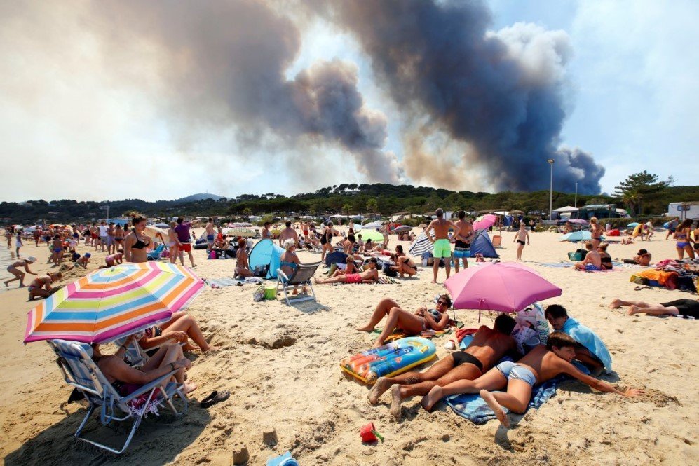 tourists stand on the beach and watch as smoke fills the sky above a burning hillside in bormes les mimosas in the var department france on july 26 2017